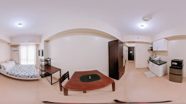 A compact living space with a bed, a dining table, a kitchenette, and an arched doorway.