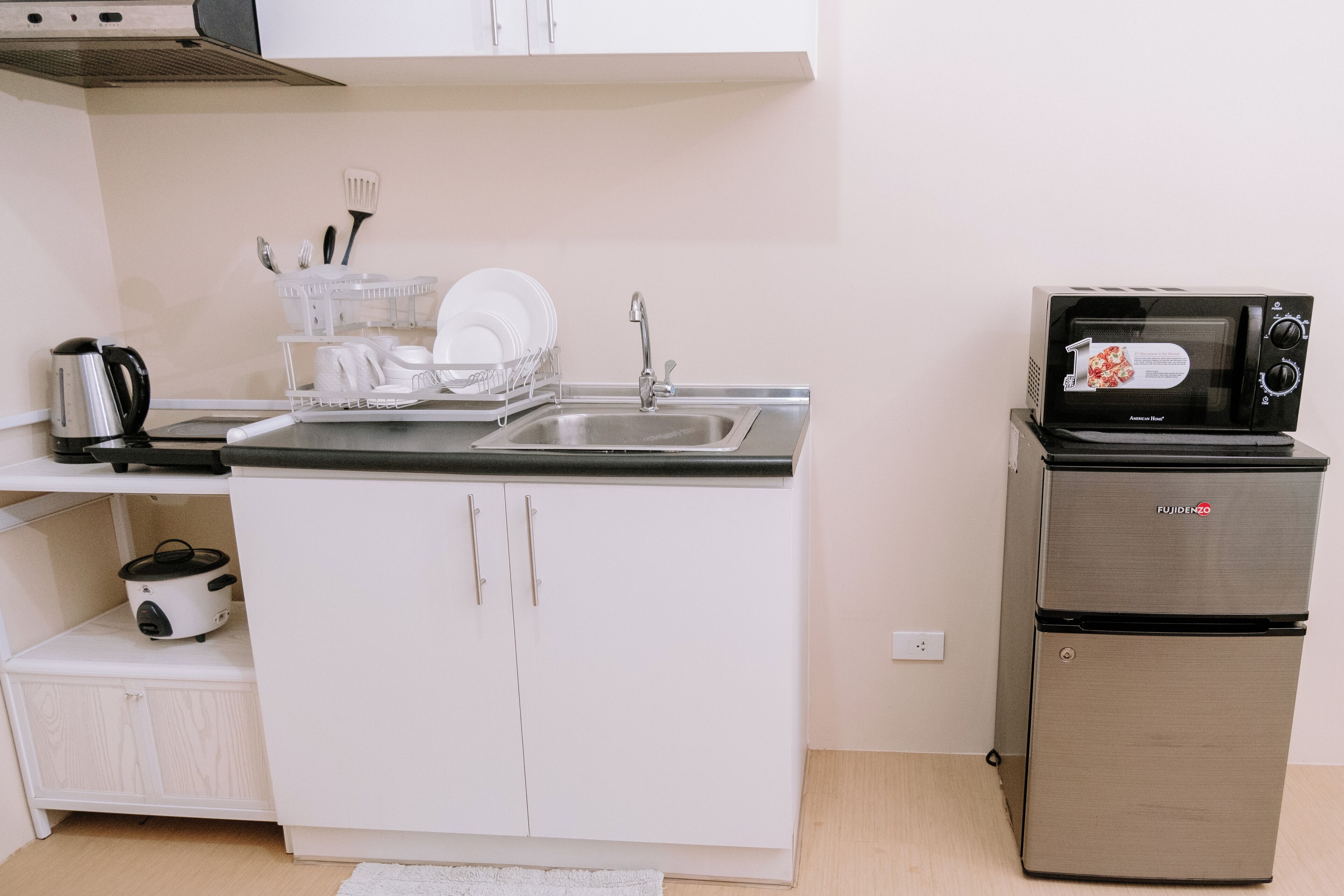 A compact kitchenette with a sink, a microwave, a small refrigerator, and a dish rack.