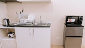 A compact kitchenette with a sink, a microwave, a small refrigerator, and a dish rack.