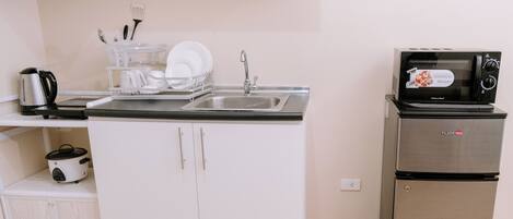 A compact kitchenette with a sink, a microwave, a small refrigerator, and a dish rack.
