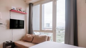 Une chambre d’hôtel avec un lit, un téléviseur fixé au mur, une petite table et une fenêtre donnant sur la ville.