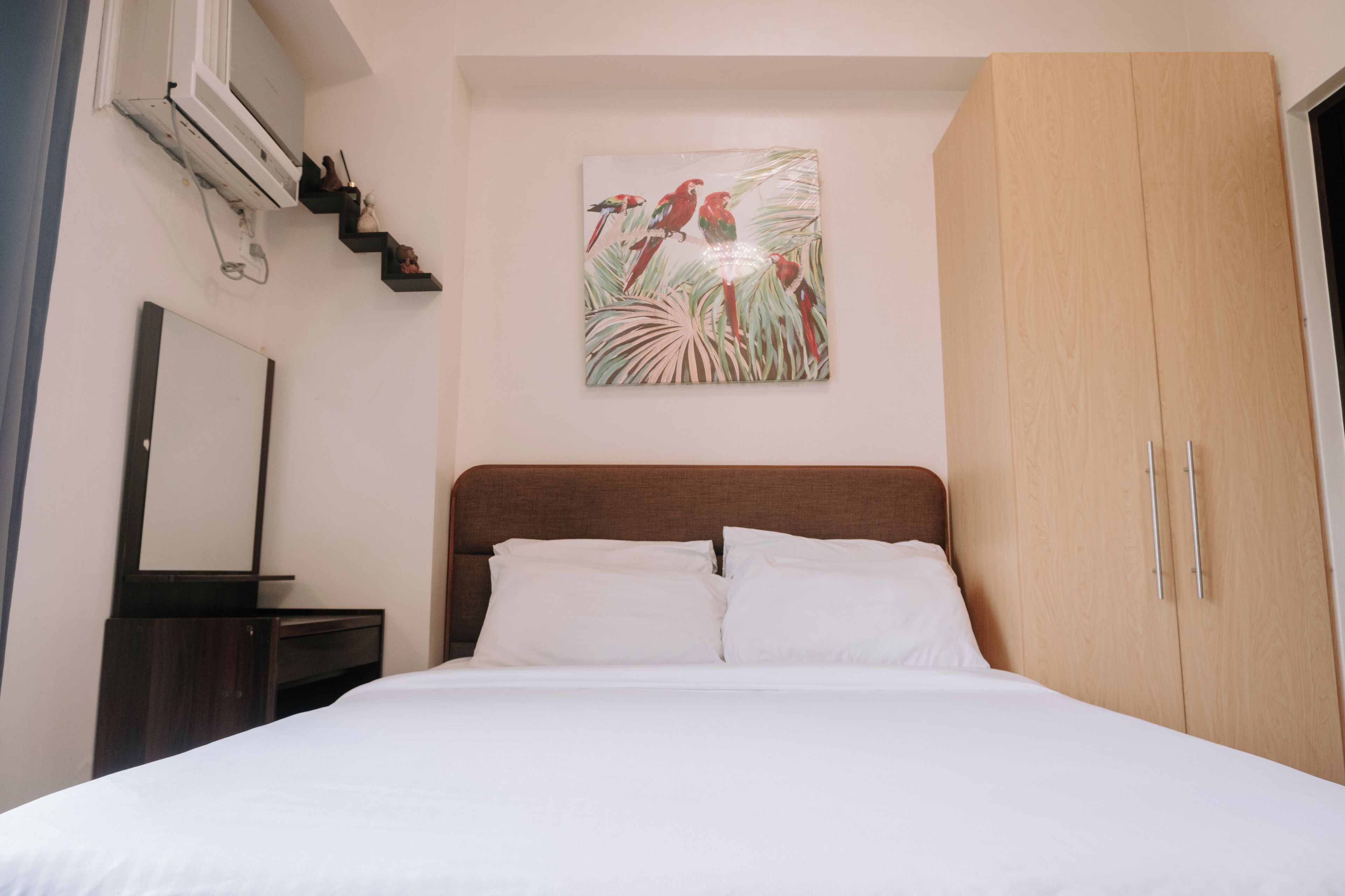 A bedroom with a bed, a wooden wardrobe, a nightstand, a mirror, and a wall-mounted air conditioner.
