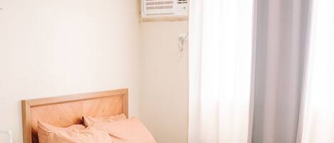 A bedroom with a wooden bed, white walls, a window with curtains, and a small table with flowers.
