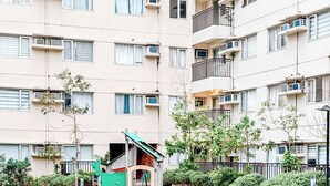 A playground with a seesaw and a slide, surrounded by a residential building with balconies and air conditioning units. - Affordable & Luxe Retreat (Iloilo)