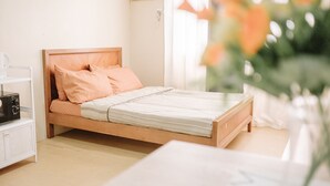 A single bed with a wooden frame and peach-colored bedding in a room with a white nightstand and a white chair. - Affordable & Luxe Retreat (Iloilo)