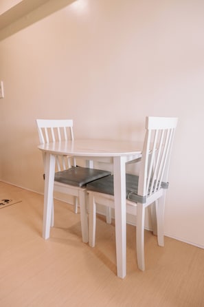 A white dining table with two chairs, a light-colored floor, and a plain wall.