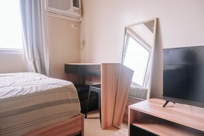 A hotel room with a bed, a desk, a TV, and a window.
