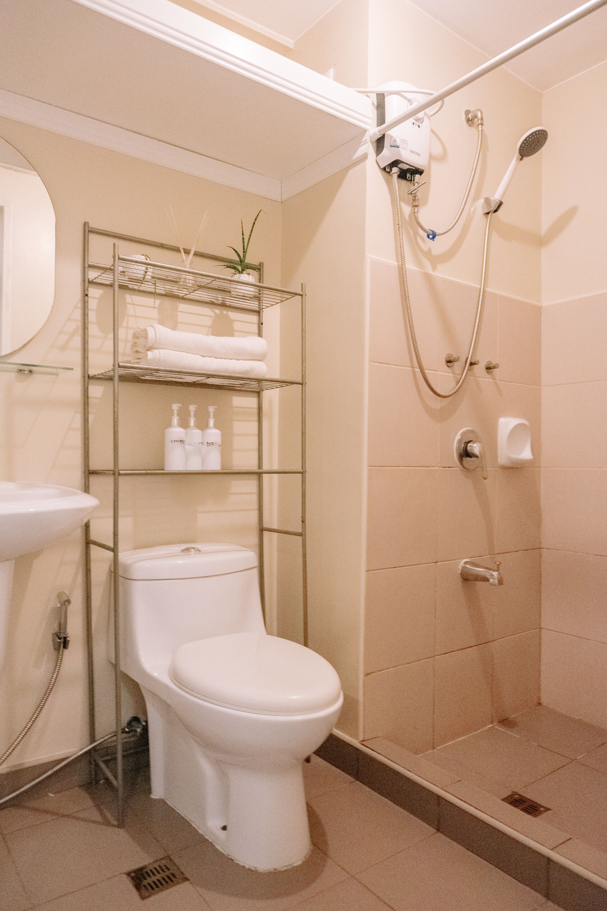A bathroom with a toilet, a sink, a shower, and a shelf with toiletries.