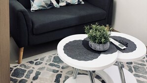 Una sala de estar moderna con un sofá negro, dos cojines estampados, una mesa de centro redonda blanca con una planta y una obra de arte enmarcada en la pared.