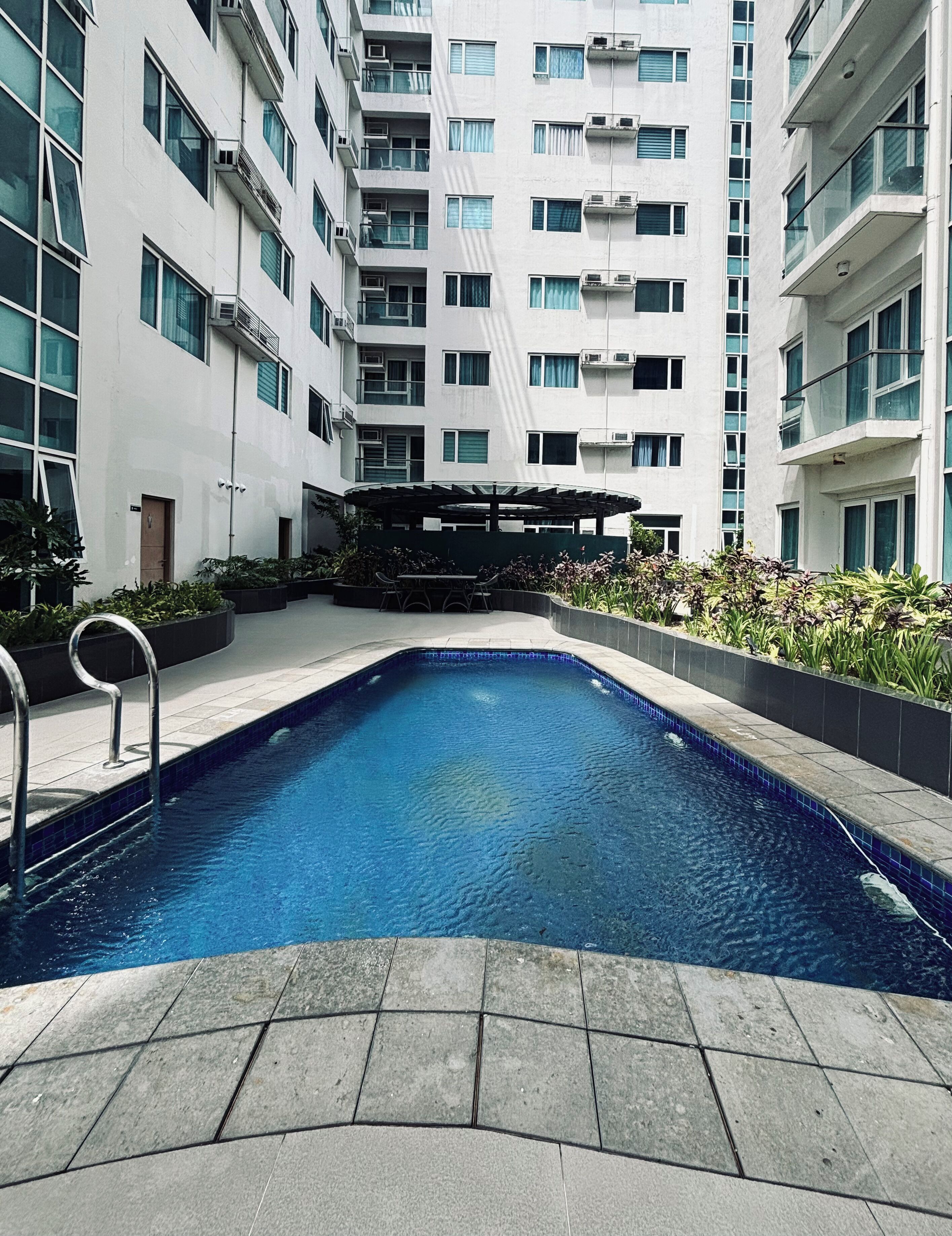 A swimming pool surrounded by a modern building with multiple balconies and a covered outdoor seating area.