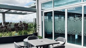 Un patio exterior con una mesa y sillas, una puerta de vidrio con diseños geométricos y vistas al cielo y las nubes.
