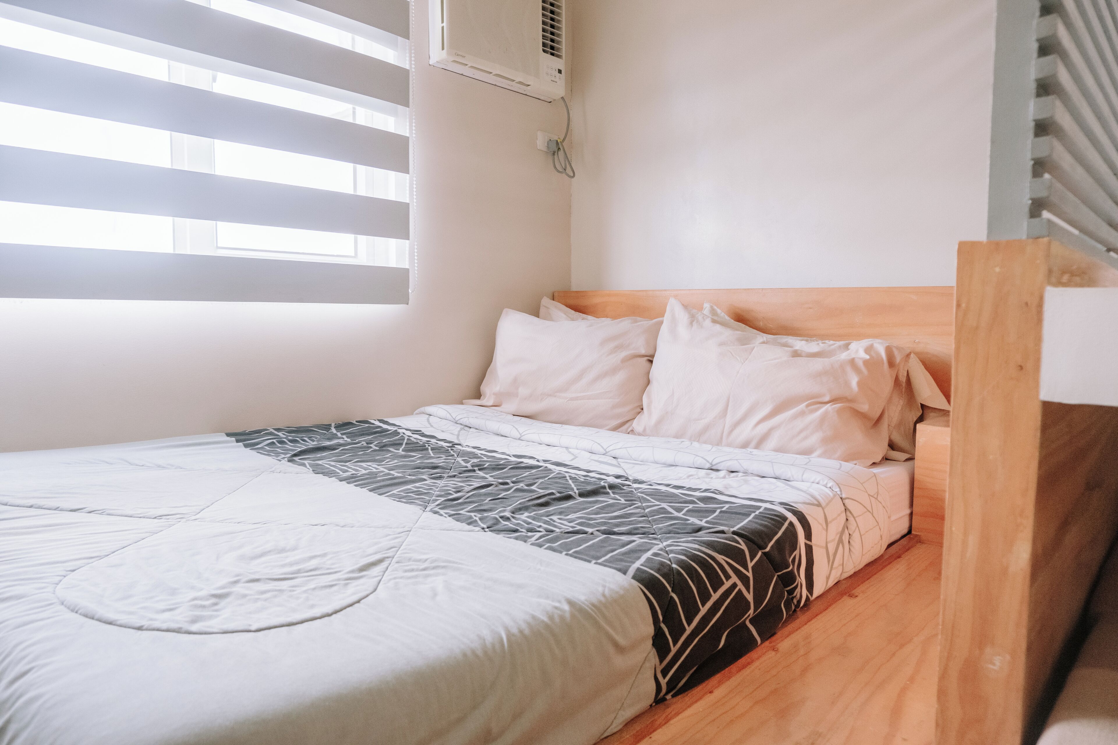 A single bed with a wooden headboard, white bedding, and a window with blinds.