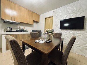 A dining area with a wooden table, four chairs, a vase with flowers, and a flat-screen TV mounted on the wall. - Barkada Getaway Near Esplanade (Iloilo)