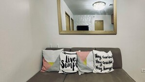 A living room with a sofa, three cushions with motivational phrases, a mirror, and a ceiling light. - Barkada Getaway Near Esplanade (Iloilo)