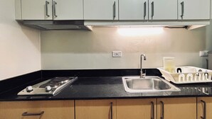 A kitchen with a black countertop, stainless steel sink, and wooden cabinets. - Your Peaceful Urban Escape (Iloilo)