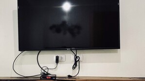 A flat-screen TV mounted on a wall with a wooden shelf below it. - Your Peaceful Urban Escape (Iloilo)