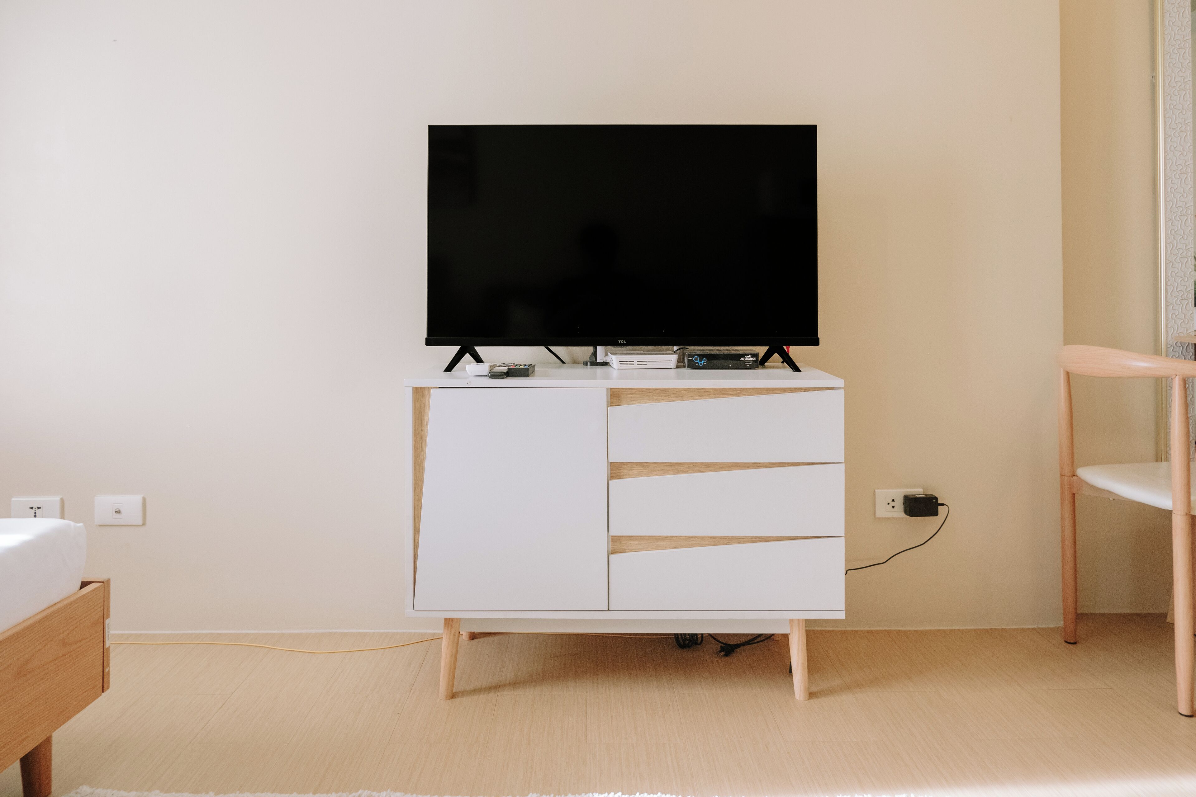 A white TV stand with a flat-screen TV, a small console, and a power outlet.