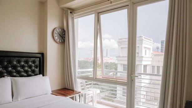 A hotel room with a bed, a clock, a balcony with a view of buildings. - Stunning Cityscape Hideout (Iloilo)