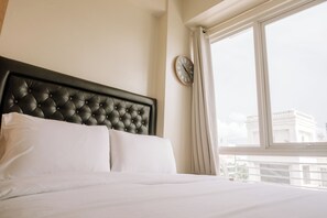 A neatly made bed with a tufted headboard, a round wall clock, and a view of a building through a window with curtains. - Stunning Cityscape Hideout (Iloilo)