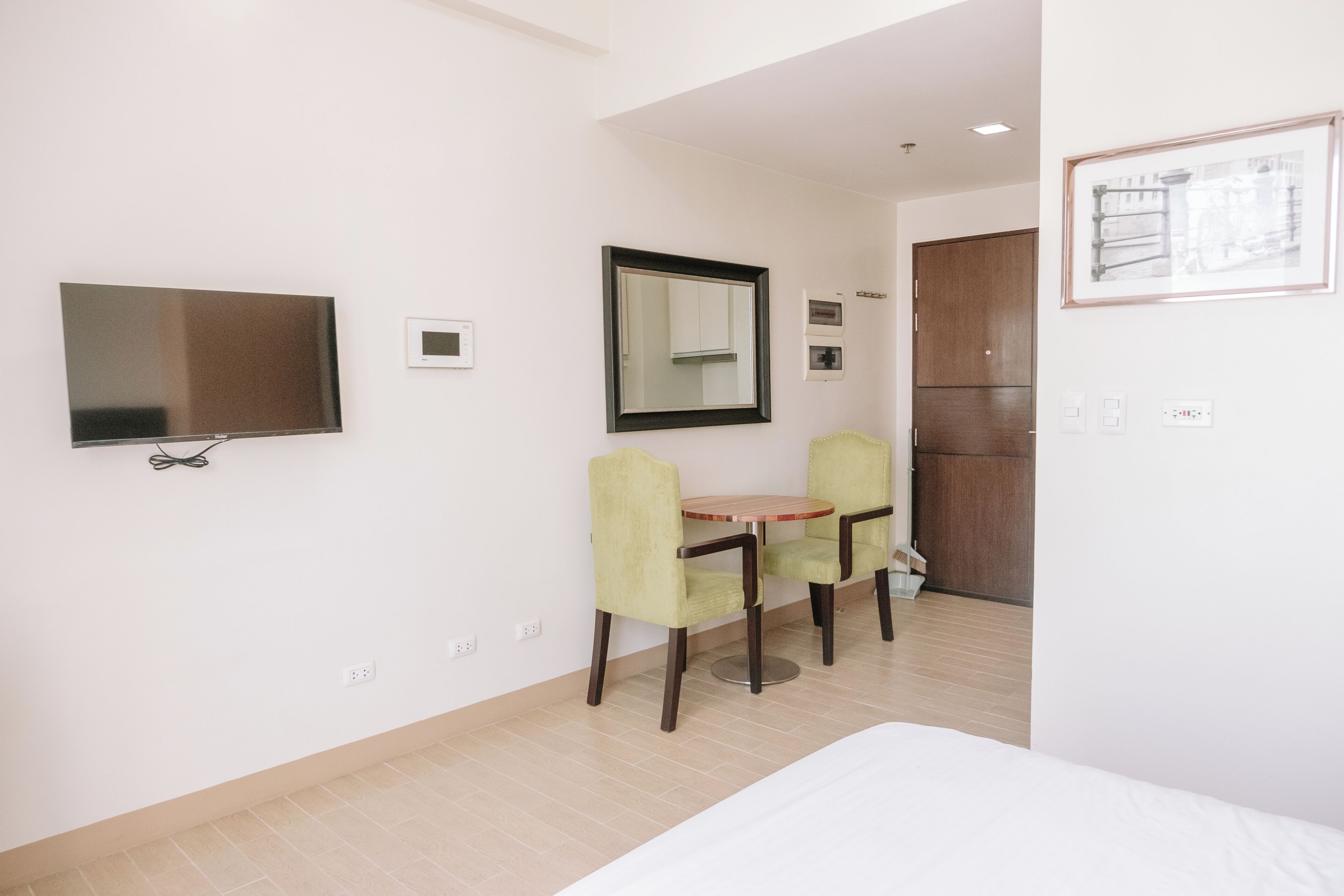 A hotel room with a bed, a TV, a small table with chairs, a mirror, and a wooden cabinet.