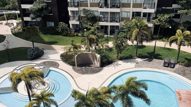 A multi-level residential building with balconies, a landscaped pool area with palm trees, and a small garden. - Chic & Stylish Urban Hideout (Iloilo)