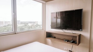 A bedroom with a bed, a TV mounted on the wall, a window, and a shelf with electronic devices. - Chic & Stylish Urban Hideout (Iloilo)