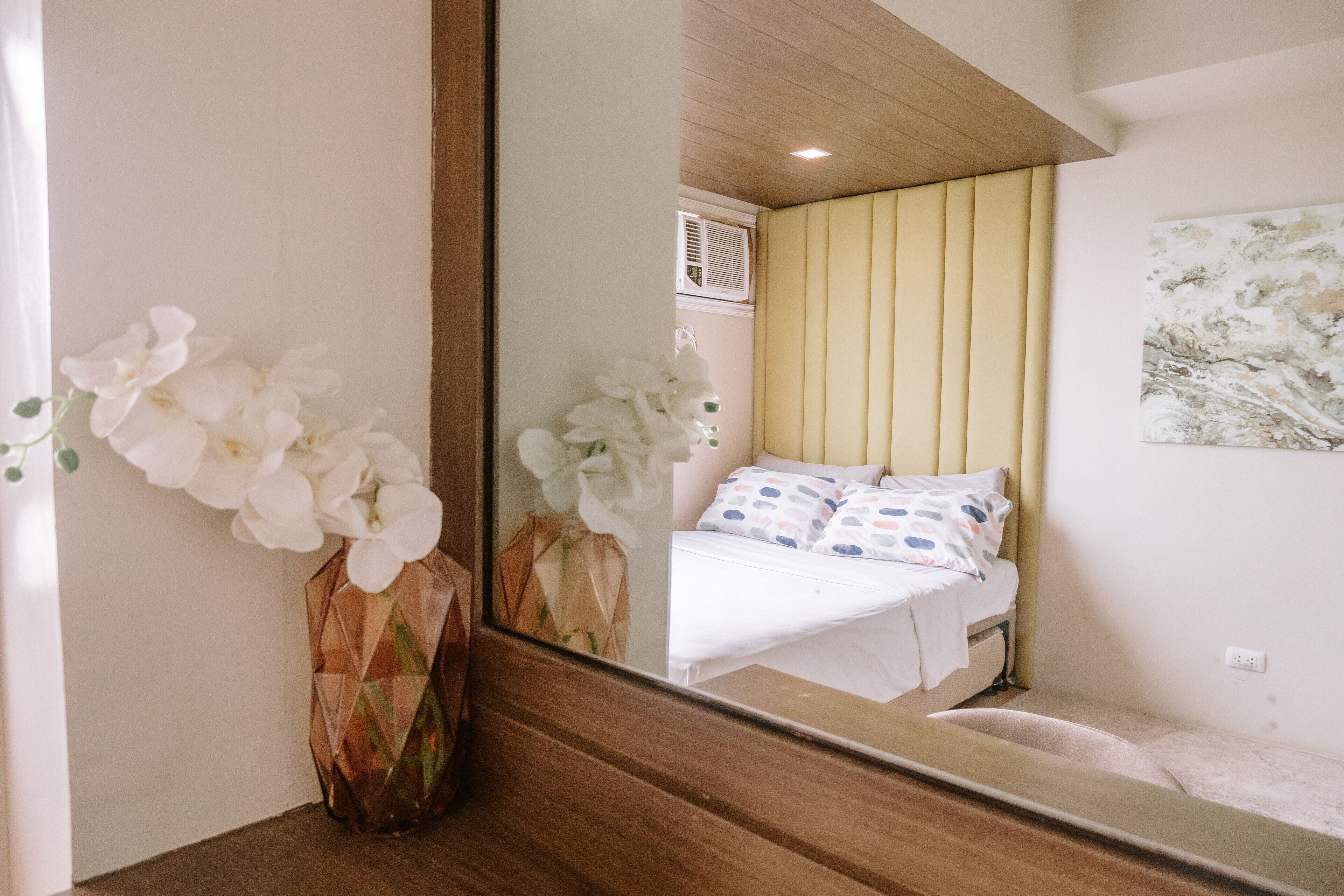 A bedroom with a bed, a mirror, and a vase with white flowers.