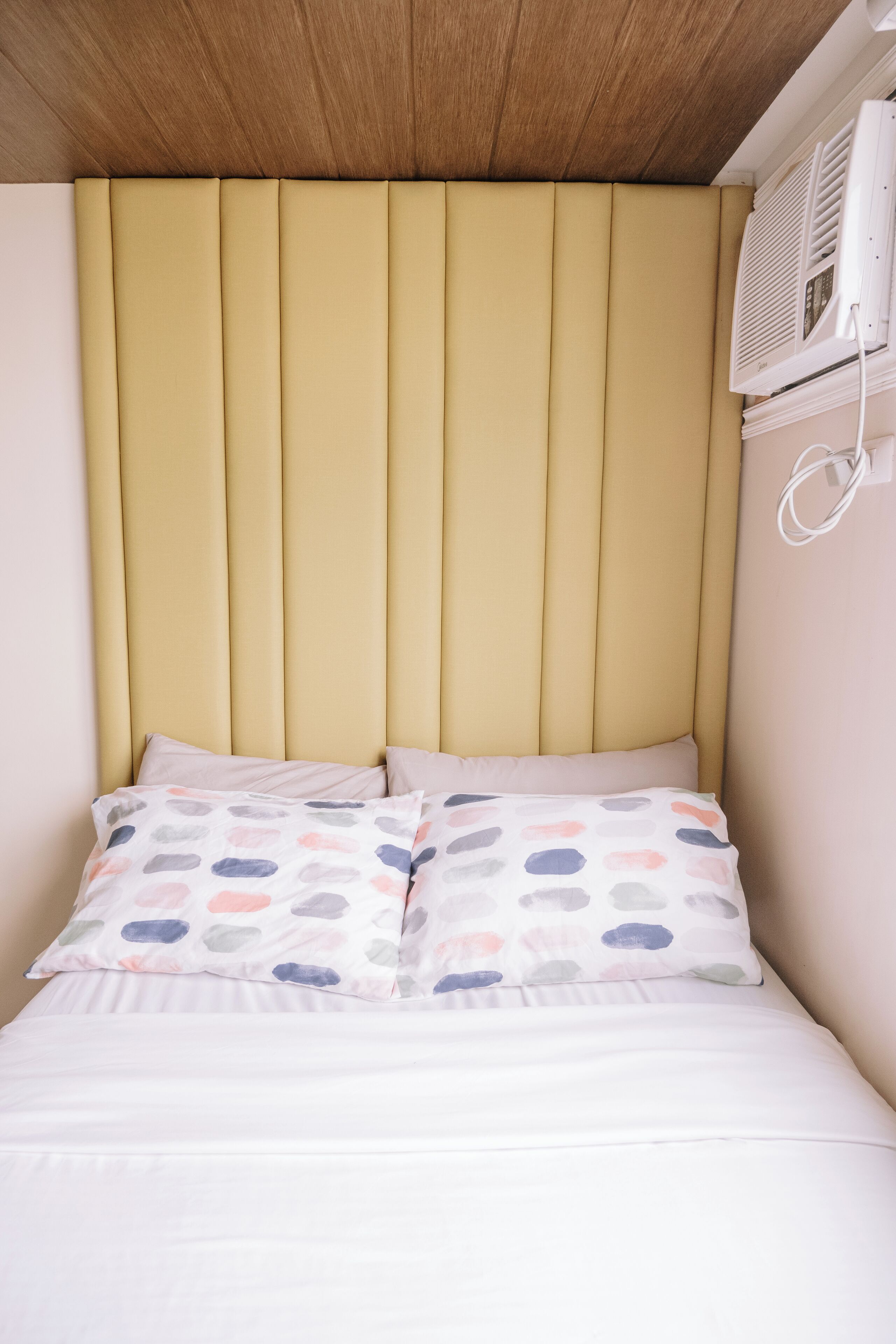 A bed with a headboard, pillows, and an air conditioning unit.