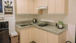 A compact kitchen with wooden cabinets, a granite countertop, a kettle, and a small potted plant. - Tropical Bliss in the Metro (Iloilo)