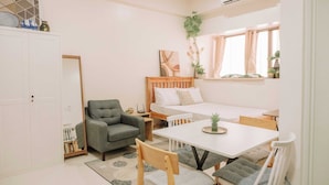 A compact, well-lit room with a bed, a dining table, a grey armchair, and a small side table. - Tropical Bliss in the Metro (Iloilo)