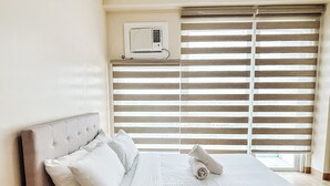 A neatly made bed with white linens and pillows, a wooden headboard, and a window with horizontal blinds. - Best Family Suite Experience (Iloilo)