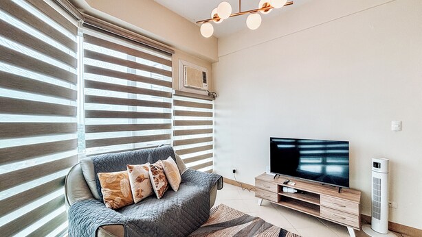 A modern living room with a sofa, TV, and a standing fan. - Best Family Suite Experience (Iloilo)