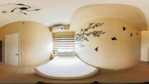 A room with a curved ceiling, a bed with white bedding, a nightstand, a dresser, and a wall with a tree and bird mural. - Playful & Charming City Loft (Iloilo)