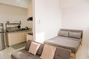 A compact living space with a kitchenette, a bed with two pillows, and a sofa with cushions. - Tranquility in the City (Iloilo)