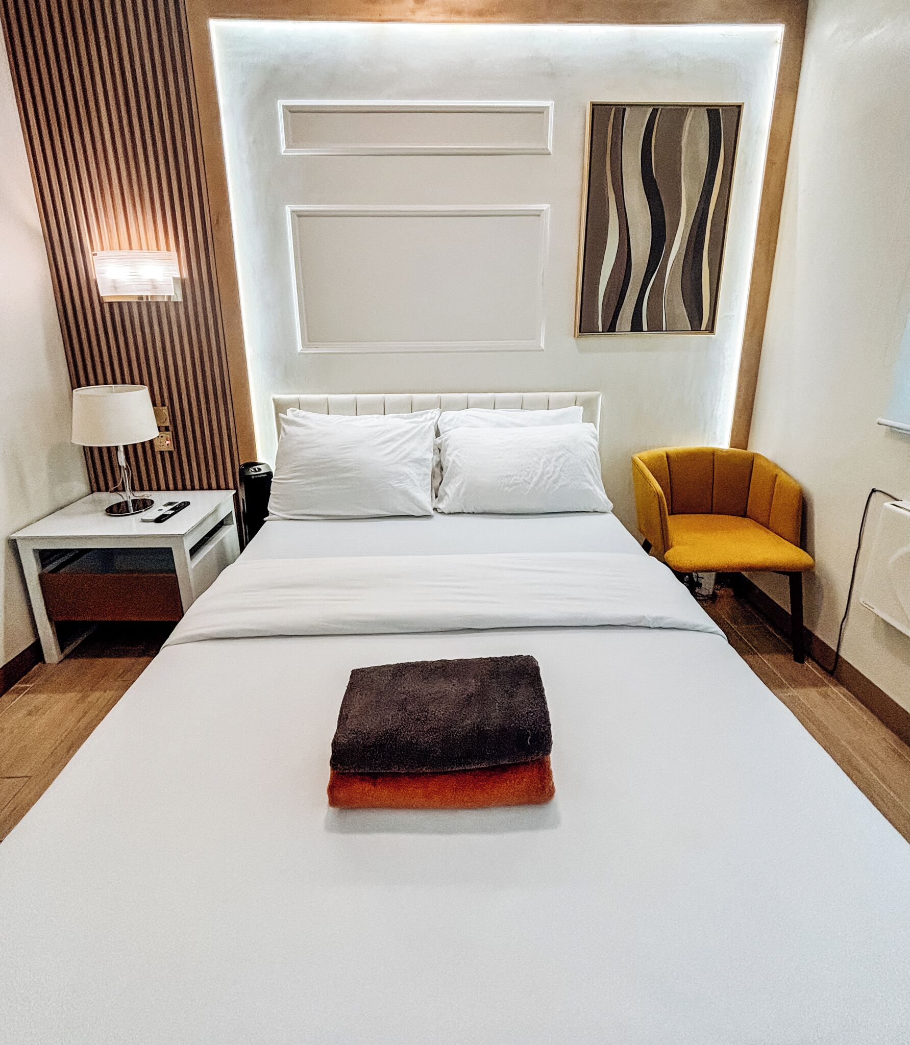 A hotel room with a large bed, a bedside table with a lamp, a chair, and a painting on the wall.