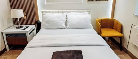 Habitación de hotel con una cama grande, una mesita de noche con lámpara, una silla y un cuadro en la pared.