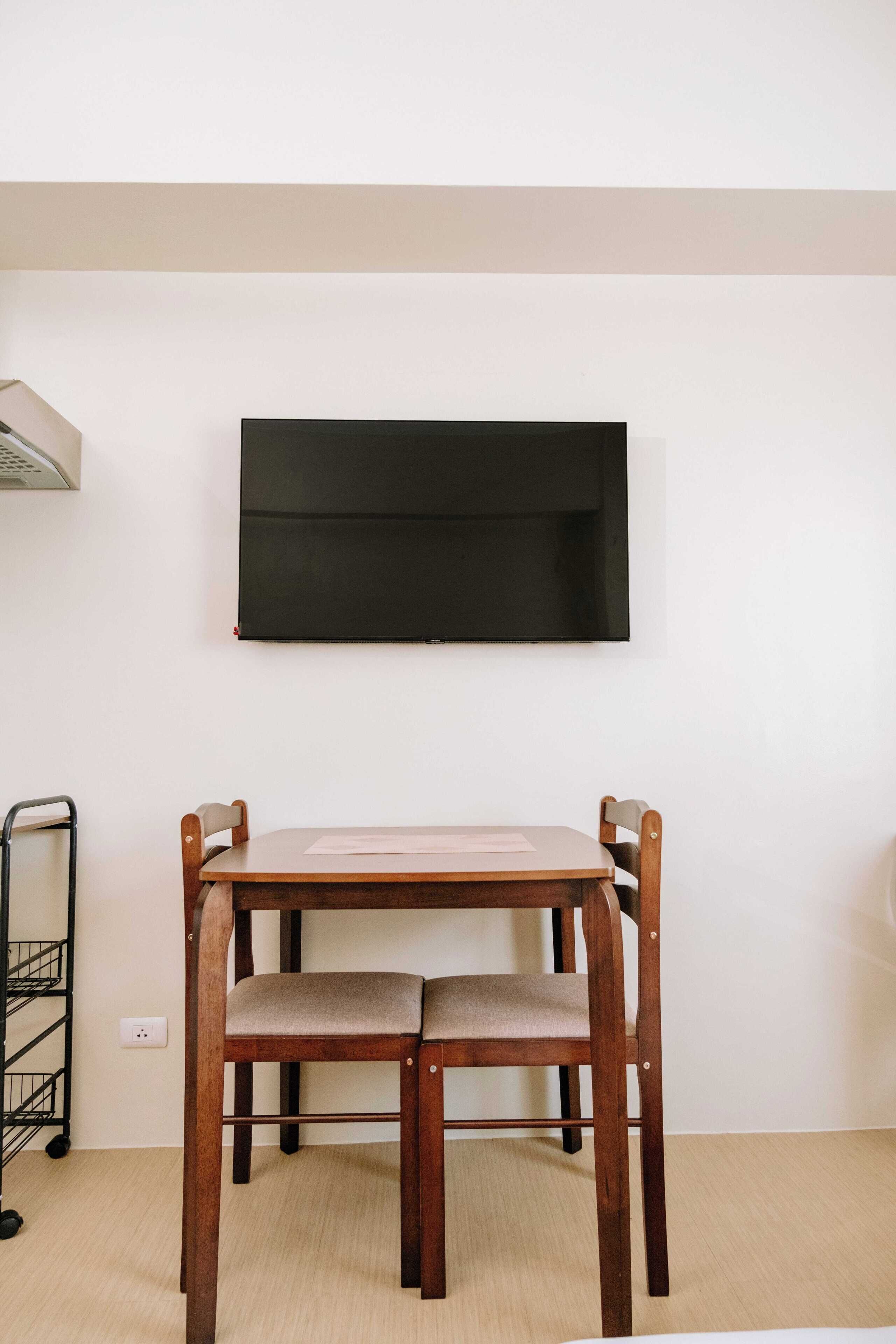 Una stanza con un tavolo e sedie in legno, una TV a parete e un carrello in metallo.