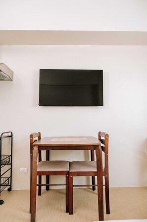 A room with a wooden table and chairs, a wall-mounted TV, and a metal cart.
