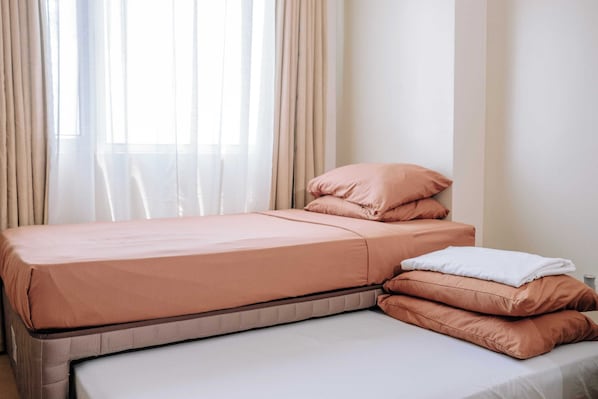 A neatly made bed with a mattress and pillows, a bedside table, and a window with curtains.