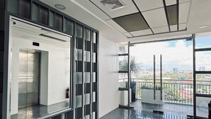 A modern interior with a glass elevator, a view of the city, and a balcony with a railing.