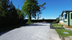 Een grindpad leidt naar een groene stacaravan met een omheinde tuin en een grote boom.