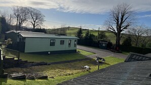 A single-story house with a green roof, a small front yard, and a hill in the background. - Cosy Grasmere Static Caravan (Natland)