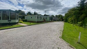 A row of green mobile homes with a gravel driveway and grassy areas. - Cosy Grasmere Static Caravan (Natland)