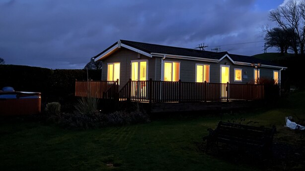 A two-story mobile home with multiple windows and a fenced backyard. - Cosy Grasmere Static Caravan (Natland)