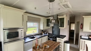 A modern kitchen with white cabinetry, a central island, a microwave, a stove, and a sink. - Cosy Grasmere Static Caravan (Natland)