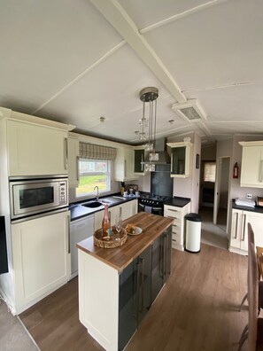 A modern kitchen with white cabinetry, a central island, a microwave, a stove, and a sink. - Cosy Grasmere Static Caravan (Natland)