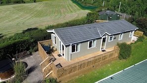 Een tweelaags huis met een terras, een omheinde tuin en een groen veld op de achtergrond.