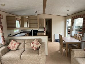 Interior compacto de autocaravana con kitchenette, un sofá con cojines estampados, una mesa de comedor y una silla.