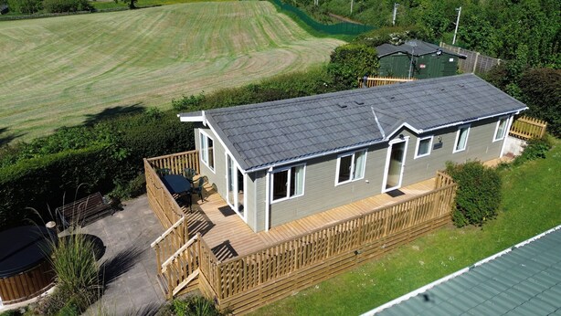 A two-story house with a deck, a fenced yard, and a green field in the background. - Cosy Rydal Static Caravan (Natland)