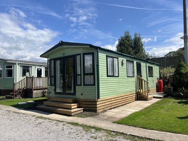 A single-story mobile home with a front porch, a small deck, and a paved driveway. - Cosy Rydal Static Caravan (Natland)
